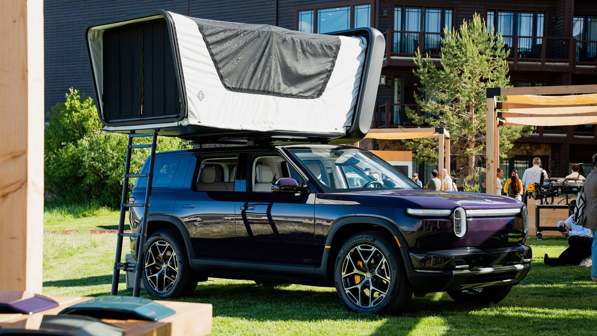 Electric SUV with rooftop tent deployed in grassy area.