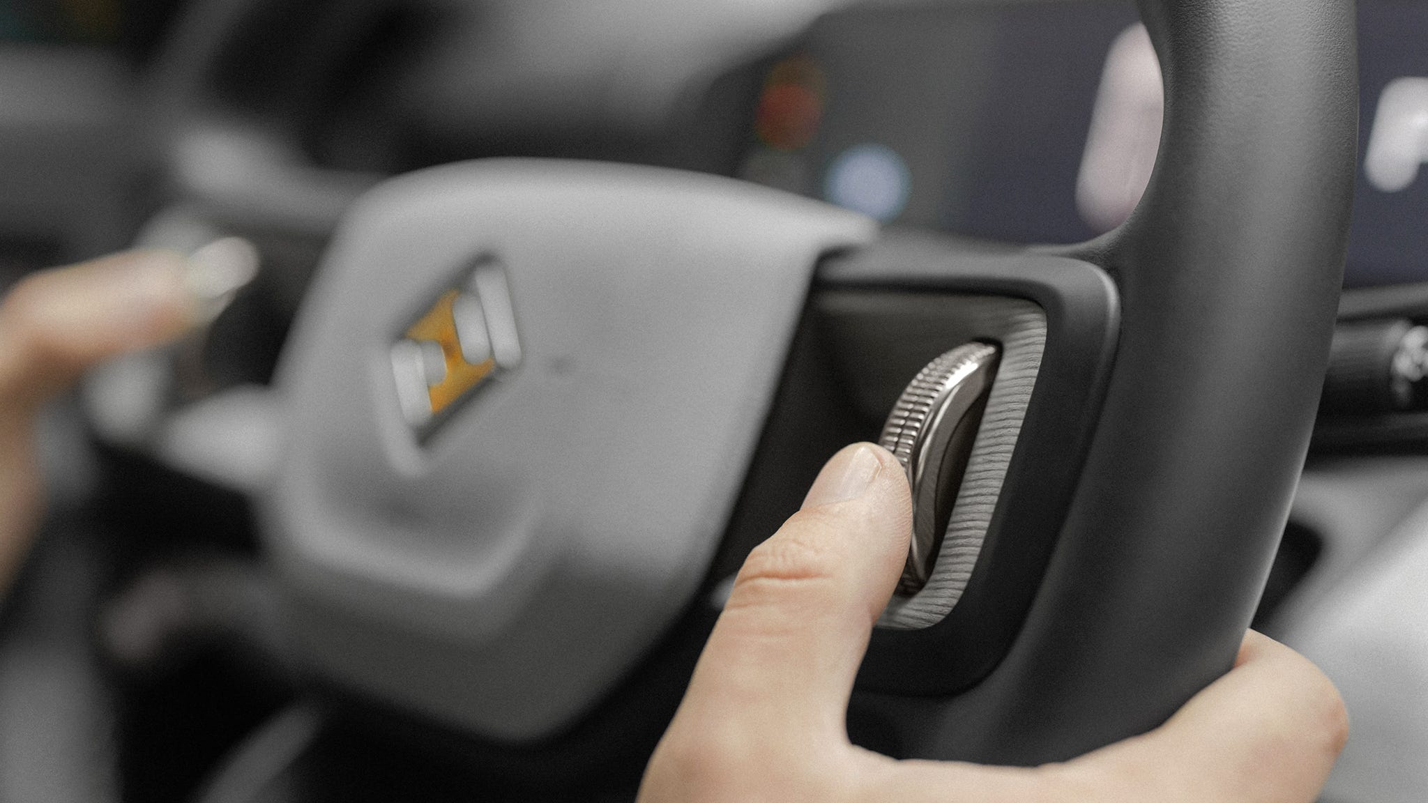 Hand adjusting a control knob on a vehicle steering wheel.