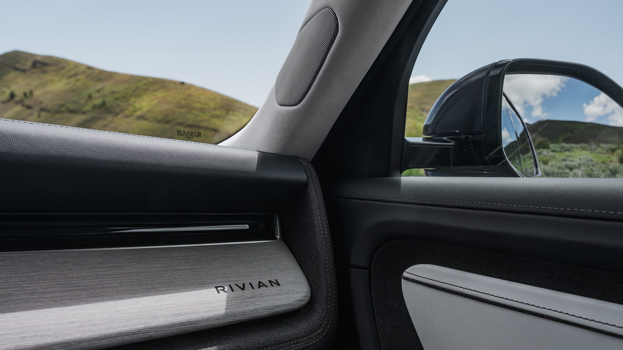 Interior view of a Rivian vehicle door and side mirror with a landscape in the background.