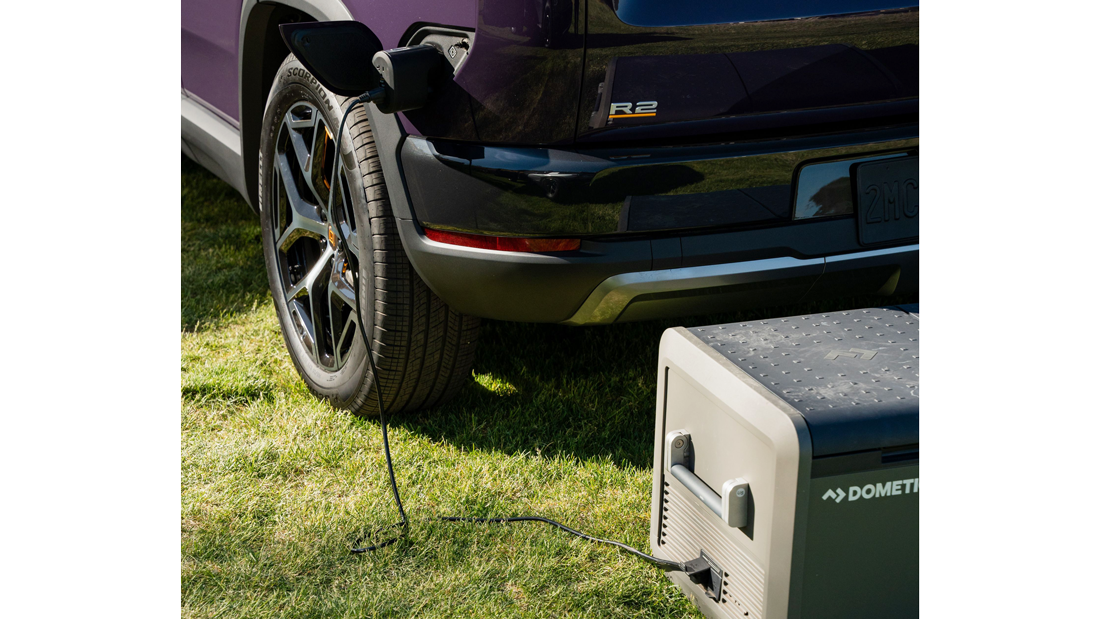 Electric car charging a portable device on grass.